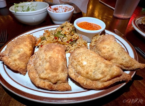 A plate of four golden-brown empanadas with a side of rice and a small bowl of dipping sauce.