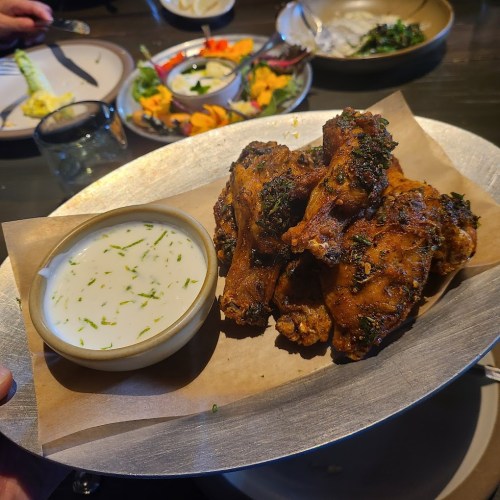 A platter of crispy chicken wings with a side of creamy dipping sauce, garnished with herbs.