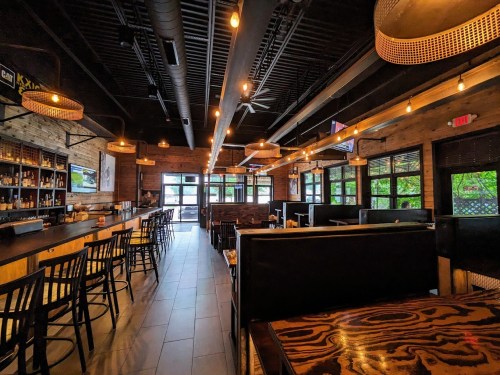 Interior of a modern restaurant featuring wooden decor, bar seating, and warm lighting.