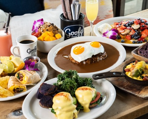 A vibrant brunch spread featuring eggs, fruit, smoothies, and various dishes on a wooden table.