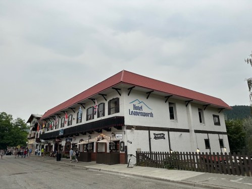 A large, two-story building with a red roof, featuring flags and a sign that reads "Hotel Leavenworth."
