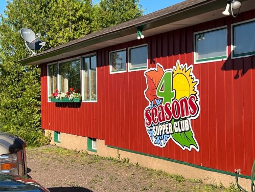 Exterior of a red building with a sign reading "4 Seasons Supper Club" and flower boxes under the windows.