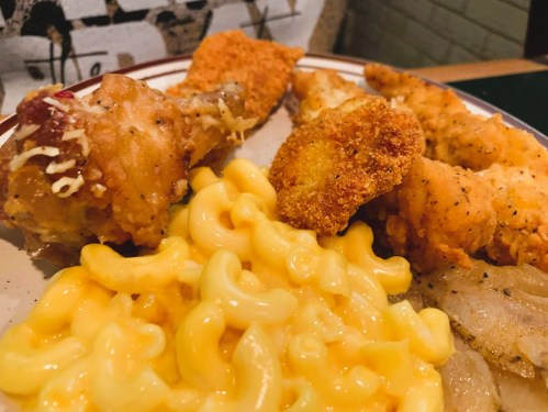A plate of fried chicken pieces, macaroni and cheese, and a golden-brown fried item.