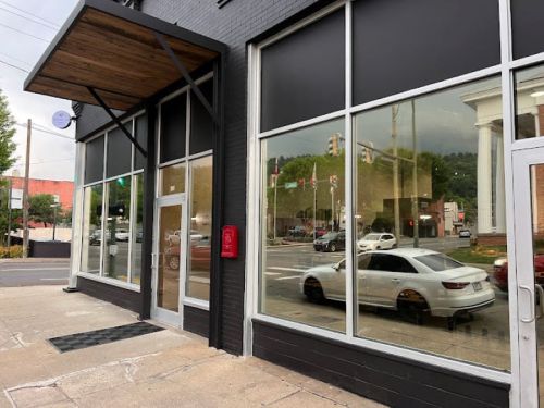 A modern building with large windows reflecting a street scene and a white car parked outside.