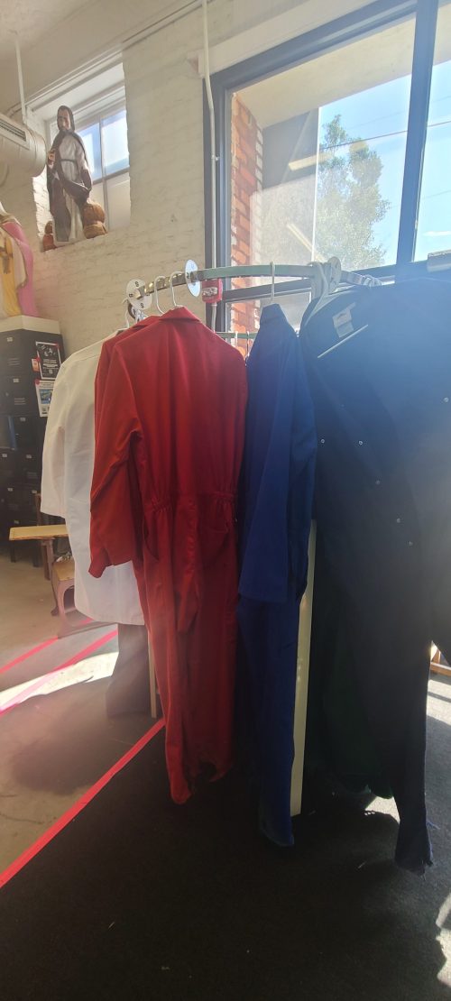 A rack of colorful work jumpsuits in red, blue, and white, with sunlight streaming through a nearby window.