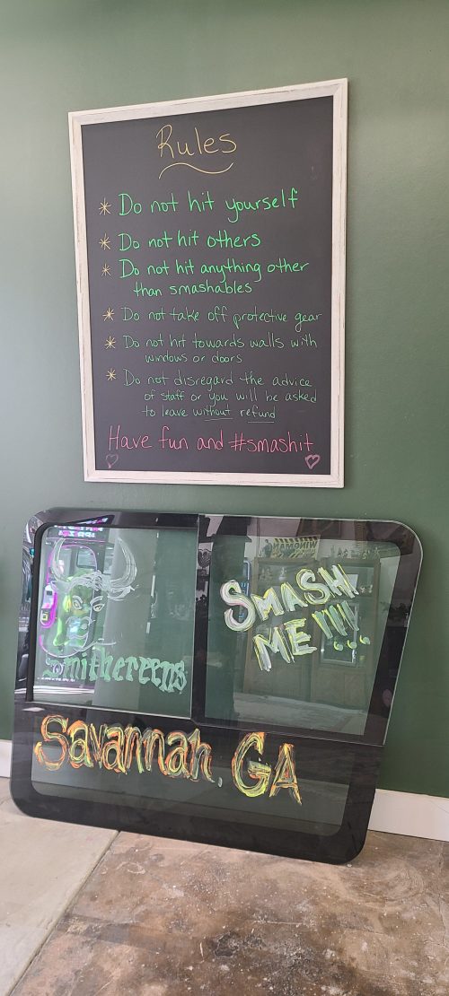 A chalkboard with rules for an activity, next to a sign that says "Savannah, GA" and "Smash Me!" on a glass panel.