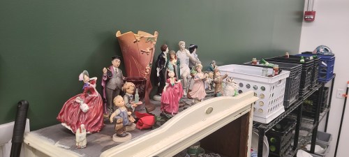 A collection of figurines and decorative items displayed on a shelf against a green wall.