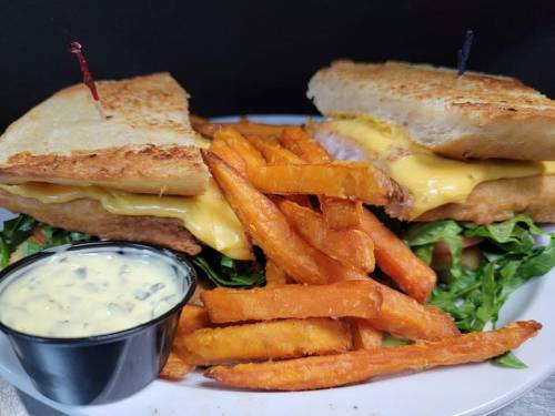 A toasted sandwich with cheese and lettuce, served with sweet potato fries and a small cup of dipping sauce.