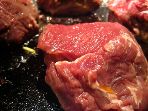 Close-up of raw red meat on a dark cooking surface, showcasing its marbled texture and freshness.