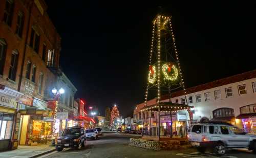 A festive street scene at night, featuring a decorated tower and shops adorned with holiday lights.