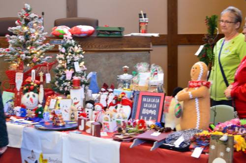 A festive display of handmade holiday crafts, decorations, and treats at a community event, with a woman observing.
