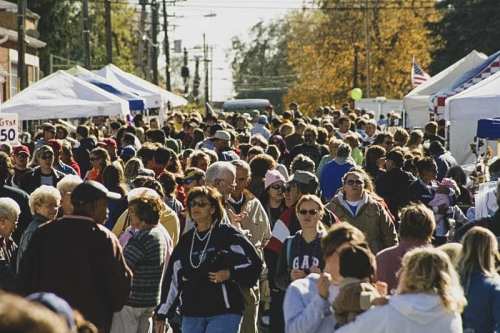 A bustling street filled with crowds of people and vendor tents during a community event or festival.