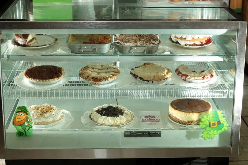 A display case filled with various desserts, including pies and cakes, with a green leprechaun decoration in front.