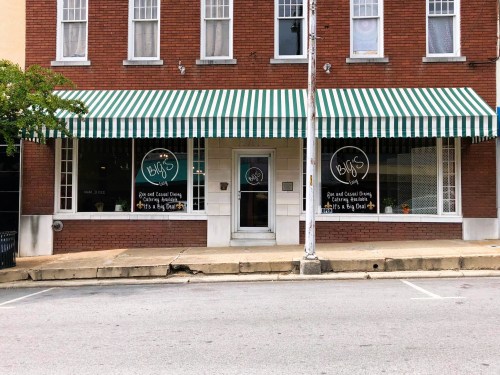 A storefront with green and white striped awnings, featuring large windows and a sign that reads "Bly's."
