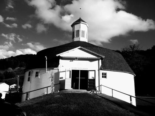 A round, white building with a cupola, set against a cloudy sky, surrounded by green hills.