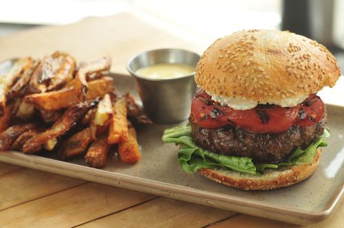 A sesame seed bun burger with lettuce, tomato, and a side of crispy fries and dipping sauce on a plate.