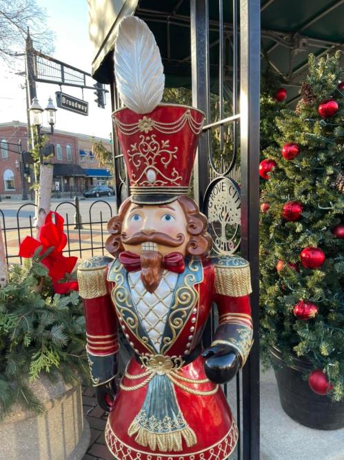 A colorful nutcracker figure stands beside a decorated Christmas tree and festive greenery.