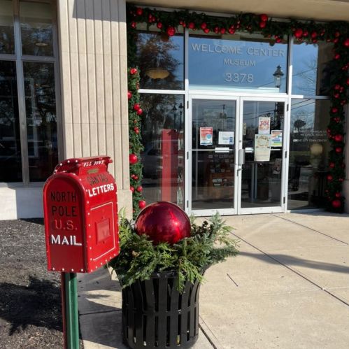 A festive welcome center entrance decorated with red ornaments and a North Pole mail box for letters.