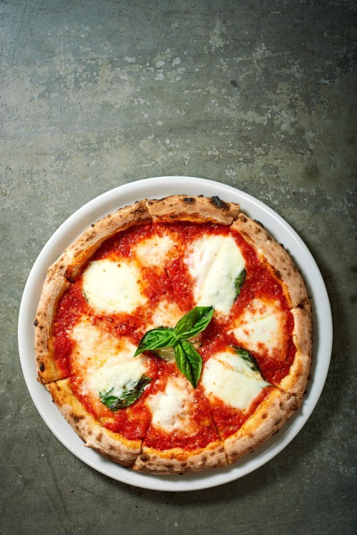 A freshly baked Margherita pizza with mozzarella, tomato sauce, and basil on a white plate.