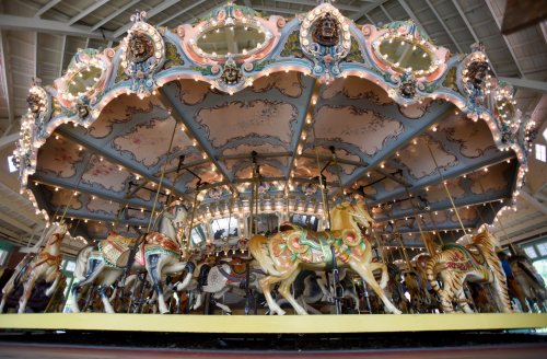 A beautifully decorated carousel with ornate horses, illuminated by lights, set under a spacious ceiling.
