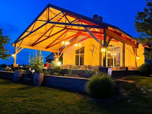 A beautifully lit outdoor patio with a wooden structure, surrounded by greenery, at dusk.