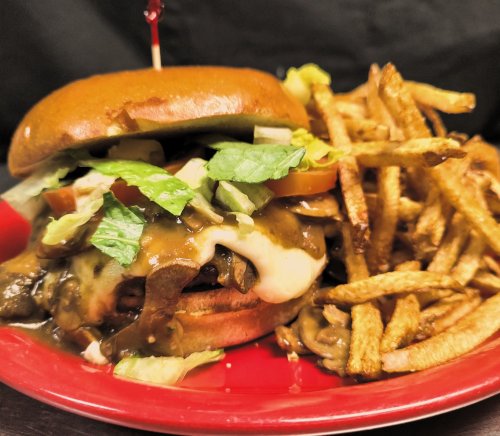 A close-up of a burger topped with lettuce, tomato, and cheese, served with a side of crispy fries on a red plate.