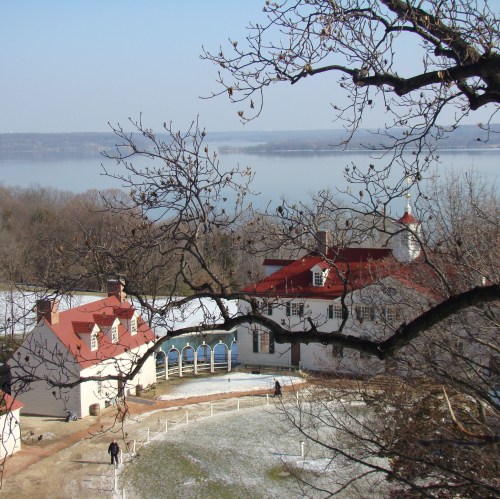 A scenic view of a historic building with red roofs, surrounded by trees and a river in the background on a clear day.