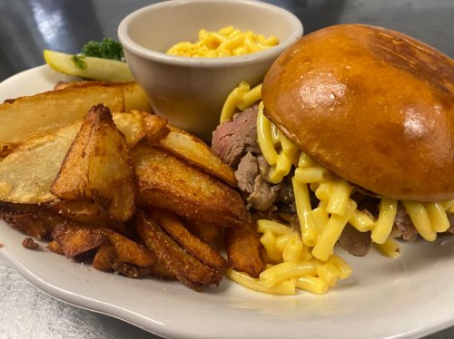 A plate featuring a sandwich with beef and macaroni, crispy potato wedges, and a side of macaroni and cheese.