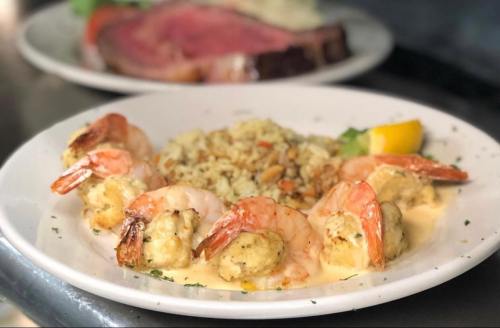 A plate of shrimp with a creamy sauce, served with rice and garnished with lemon, in a restaurant setting.