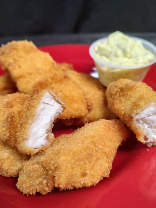 A plate of golden-brown chicken tenders with a small cup of creamy dipping sauce.