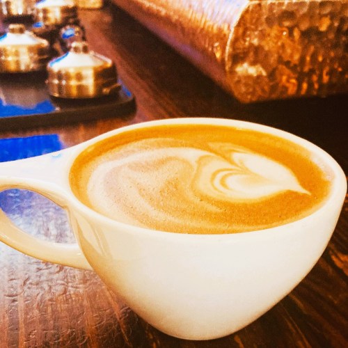 A close-up of a latte in a white cup, featuring a creamy swirl design, on a wooden table.