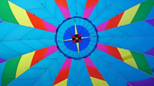 Colorful hot air balloon canopy viewed from below, featuring vibrant blue, yellow, pink, and green patterns.