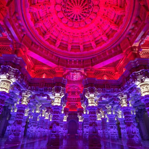Vibrant interior of a temple with intricate columns and a colorful, illuminated ceiling.