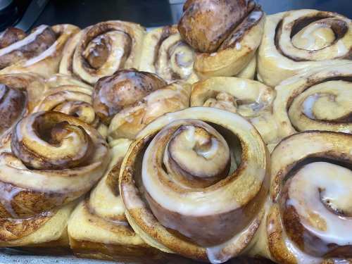 A close-up of freshly baked cinnamon rolls drizzled with icing, arranged in a baking tray.