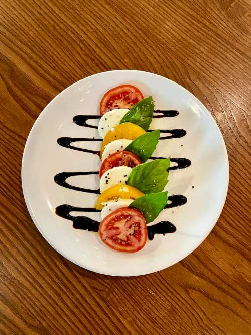 A plate of Caprese salad with sliced tomatoes, mozzarella, basil, and balsamic drizzle on a wooden table.