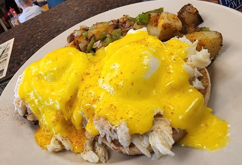 A plate of eggs Benedict with poached eggs and hollandaise sauce, served with seasoned potatoes and vegetables.