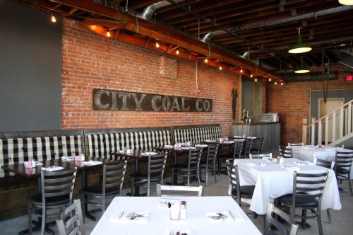 Interior of a restaurant with brick walls, wooden beams, and checkered seating, featuring tables set for dining.