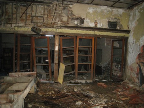 An abandoned, dilapidated room with broken furniture, peeling walls, and dusty shelves.