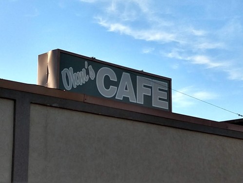 Sign for "Owen's Cafe" against a blue sky, mounted on a building.