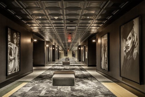 A long hallway with dark walls, large black-and-white portraits, and benches, featuring a patterned ceiling.