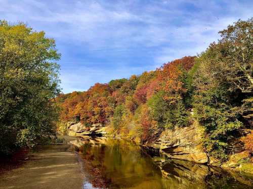 A serene river flows through a landscape of vibrant autumn foliage and rocky cliffs under a clear blue sky.