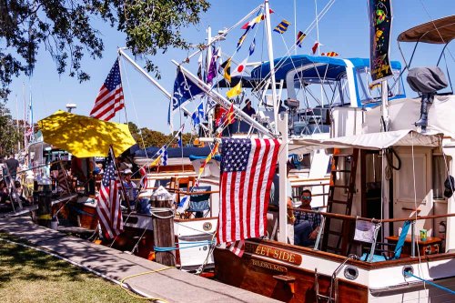 Colorful boats decorated with flags and American banners docked along a sunny waterfront.