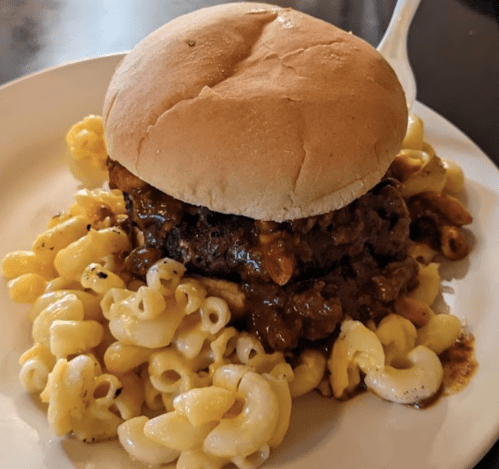 A hamburger topped with a savory sauce, served on a plate with a side of macaroni pasta.