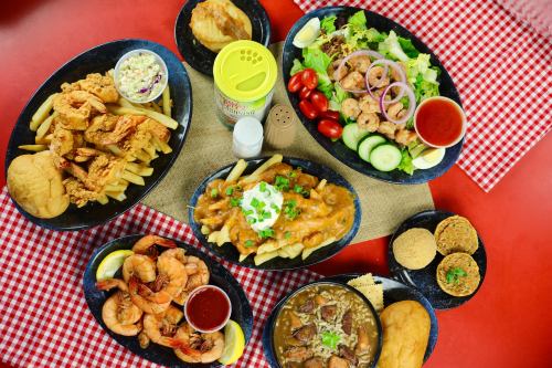 A spread of various dishes including shrimp, fries, salad, and sides on a checkered tablecloth.