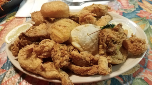 A plate of fried chicken, biscuits, and a slice of lemon on a colorful tablecloth.