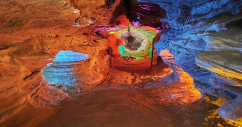 A colorful cave interior with vibrant lighting illuminating the rock formations and sandy floor.