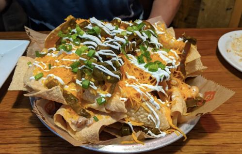 A plate of nachos topped with cheese, jalapeños, green onions, and sour cream on a wooden table.