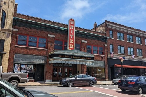 Historic theater with "United" marquee, red windows, and a blue sky above, surrounded by brick buildings and parked cars.