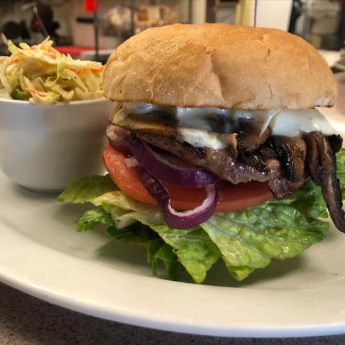 A juicy burger with lettuce, tomato, grilled onions, and mayonnaise, served with a side of coleslaw.