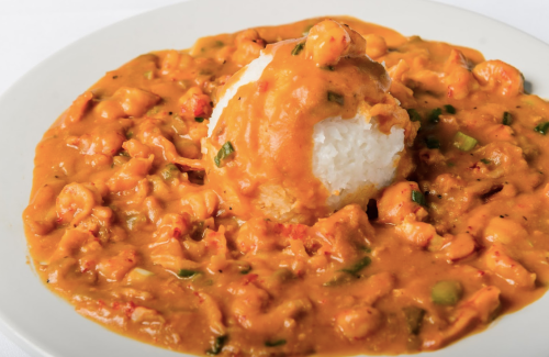 A plate of creamy shrimp stew served over a mound of white rice, garnished with green onions.